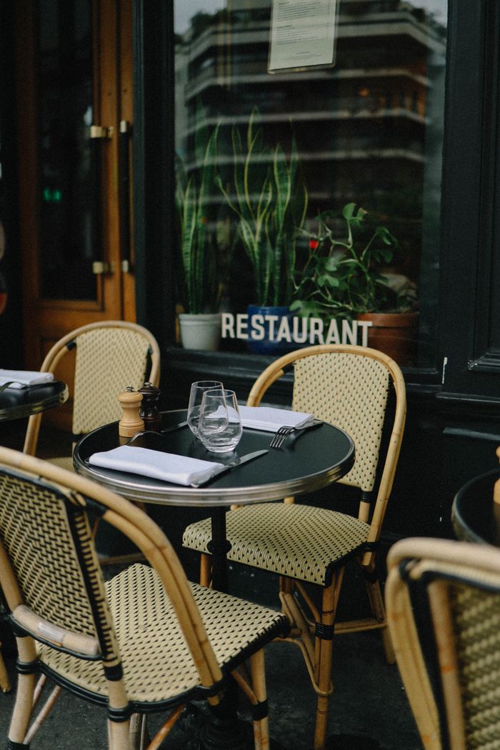 about-img Charming outdoor restaurant setting with wicker chairs and tableware, ideal for al fresco dining.