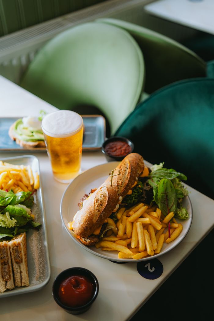 services-01 Plate with sandwich, fries, and beer in a cozy cafe setting.