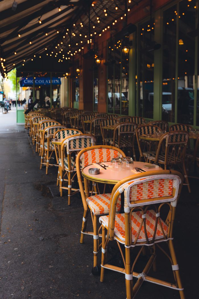 gallery-3 Cozy urban sidewalk cafe with wicker chairs, tables, and string lights.