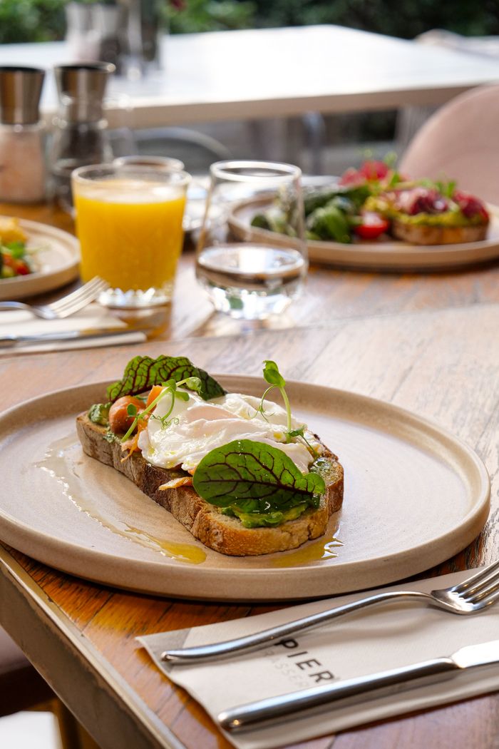 services-03 Delicious gourmet breakfast toast with poached egg and greens, served with juice in a café setting.