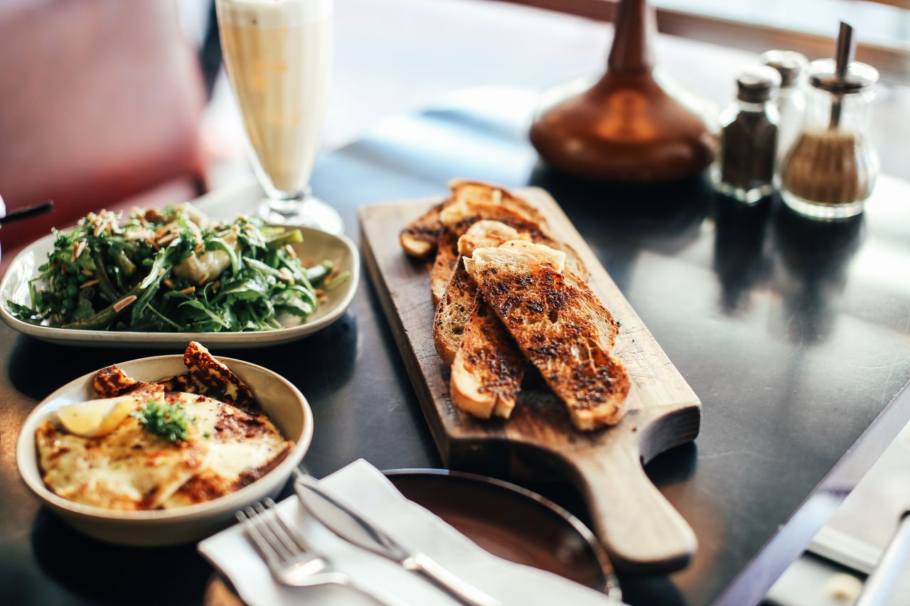 gallery-1 A delicious breakfast setup with toast, salad, and a smoothie on a wooden cutting board, perfect for brunch.