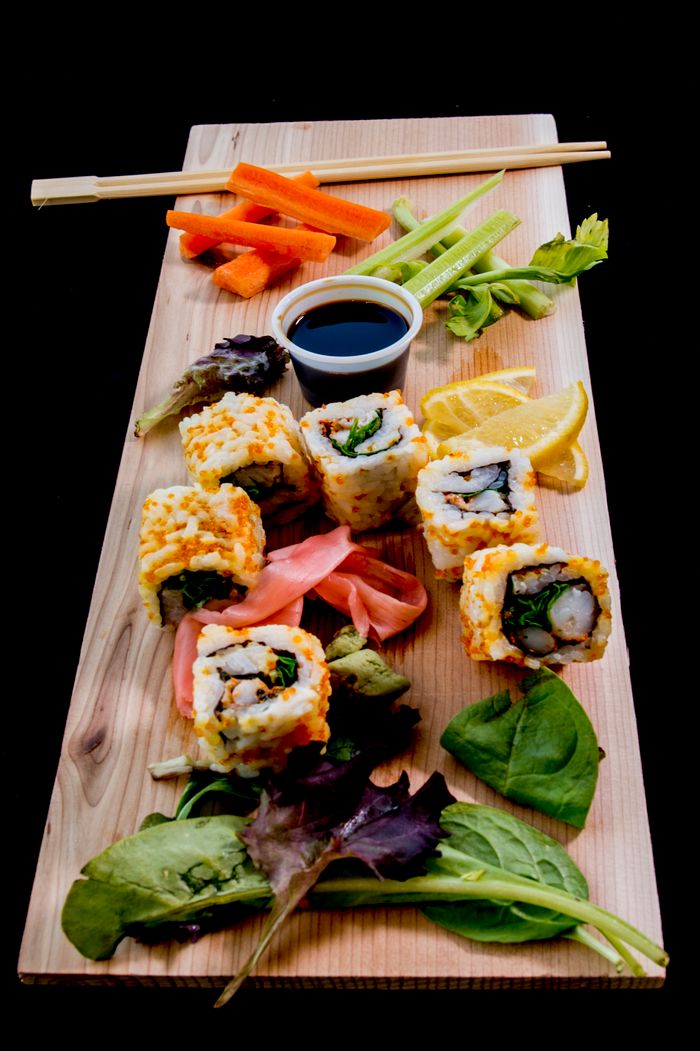 contact-img Vibrant sushi platter with fresh vegetables and soy sauce on a wooden board.