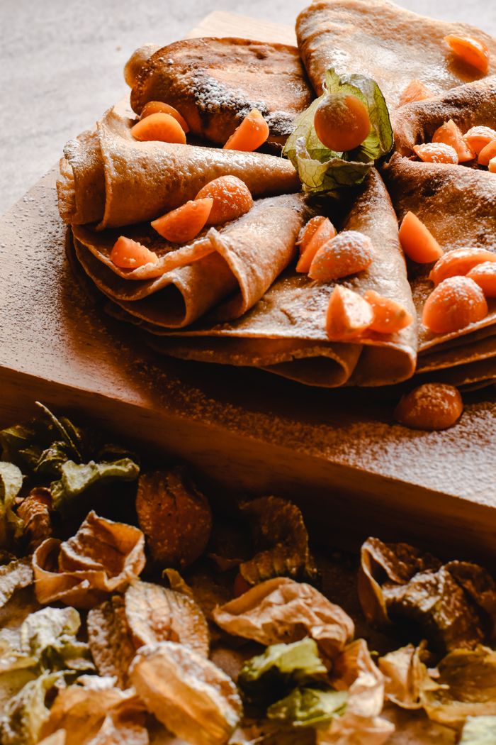 services-img Indulge in gourmet pancakes topped with cape gooseberries, beautifully presented on a rustic wooden board.